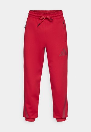 Pantalon de survêtement athlétique rouge avec taille élastique, cordon de serrage ajustable, poches latérales zippées et logo adidas dans une teinte contrastante.