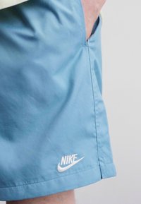 Calções Nike de cor azul claro, feitos de um tecido suave, apresentando um pequeno logótipo branco na bainha, com bolsos laterais e um corte descontraído.