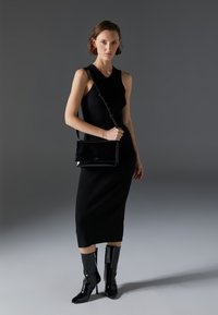 Black ribbed knit dress, knee-length. Glossy black handbag with a strap, and high-shine black knee-high boots with zip detail.