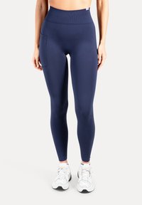 Marineblauwe leggings met hoge taille gemaakt van rekbare stof, voorzien van een zijzak en een gladde textuur, gecombineerd met witte sportschoenen.