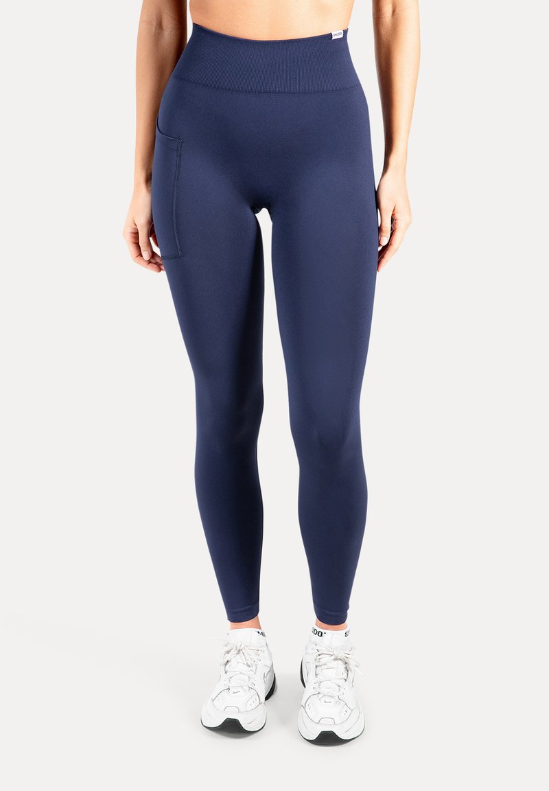 Marineblauwe leggings met hoge taille gemaakt van rekbare stof, voorzien van een zijzak en een gladde textuur, gecombineerd met witte sportschoenen.