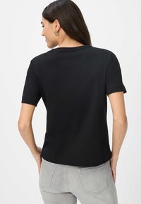 Schwarzes T-Shirt mit kurzen Ärmeln und Rundhals, aus glattem Baumwollstoff, mit entspannter Passform und dezenten Nähten an den Ärmeln.