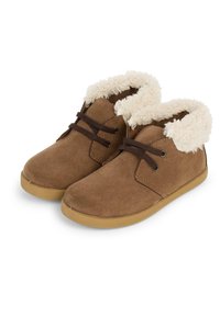 Botas de tobillo de ante marrón con un forro de piel sintética color crema, cordones marrones y una suela de goma flexible. Diseño de punta redondeada con una textura suave.