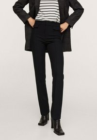 Pantalon noir ajusté avec une coupe slim, doté de poches avant, d'une texture lisse et d'une taille haute. À associer avec un haut rayé et un blazer.