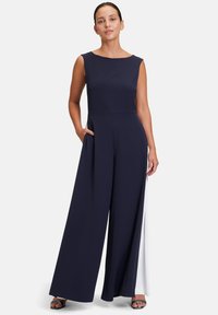 Combinaison sans manches bleu marine avec un corsage ajusté, un design à jambes larges, des poches latérales et un panneau latéral blanc contrastant. Texture de tissu lisse.