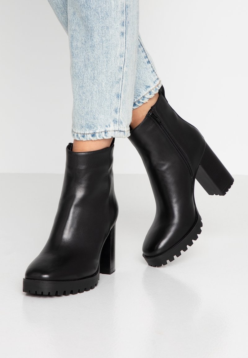 Mustat nahka nilkkurit, joissa on paksu korko, pyöreä kärki ja vetskariyksityiskohta. Ulkopohja on varustettu kuvioinnilla paremman pidon saavuttamiseksi.