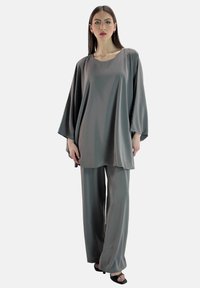 Graues Satin-Tunikaset und weite Hosen, das sich durch eine lockere Passform, lange Ärmel und eine glatte Textur auszeichnet, ergänzt durch minimalistisches schwarzes Schuhwerk.