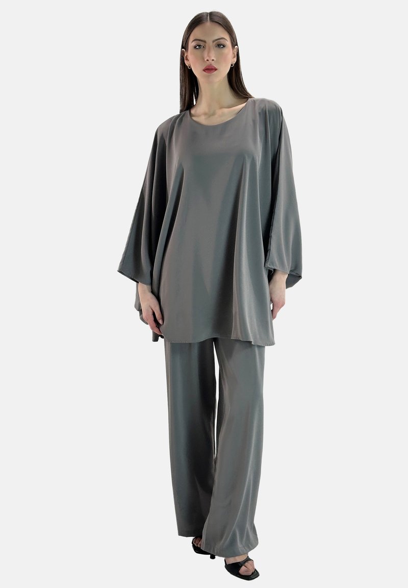 Graues Satin-Tunikaset und weite Hosen, das sich durch eine lockere Passform, lange Ärmel und eine glatte Textur auszeichnet, ergänzt durch minimalistisches schwarzes Schuhwerk.