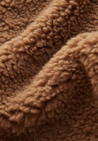 Gros plan sur un tissu polaire doux, marron et texturé avec des fibres épaisses et bouclées visibles et des plis délicats.