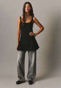 Top nero senza maniche con un design svasato, abbinato a jeans grigi sbiaditi a gamba larga e scarpe con platform nere. Texture del tessuto liscia.