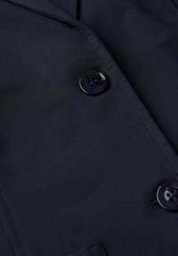 Námořnický blazer s hladkou texturou, dvěma tmavými knoflíky a klopou s výřezem. Disponuje čistým šitím a přiléhavým střihem.