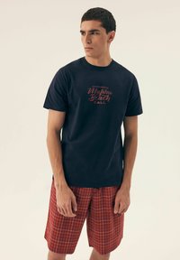 Czarna koszulka w kolorze granatowym z czerwoną grafiką "Malibu Beach", w połączeniu z szortami w czerwono-białą kratkę. Materiał bawełniany, swobodny krój.