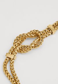 Collana in oro con maglie intrecciate, finitura lucida e due accenti del logo "GUESS" in oro. Design texturizzato e intricato.