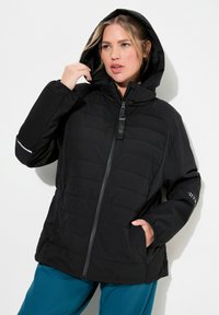 Chaquetón negro acolchado con capucha, con cremallera frontal, dos bolsillos laterales y detalles reflectantes en las mangas. Textura mate.