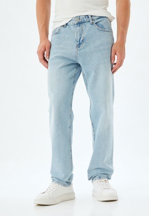 Jeans de denim azul claro con un diseño de pierna recta, estilo de cinco bolsillos, cierre de botón y textura desvanecida. Llevados con zapatillas blancas.