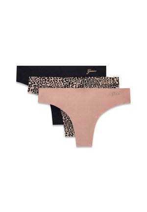 Femme aux longs cheveux noirs portant un soutien-gorge noir à bordure en dentelle, une culotte taille haute assortie et des talons dorés à lanières, debout devant un fond clair.