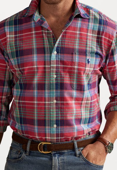 Sarkans un zils kostīms ar zaļām akcentiem, garām piedurknēm, pogu apkakli un krūšu kabatu. Nēsāts ar brūnu jostu un pulksteni.