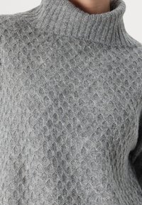 Pull en tricot gris avec un col montant côtelé, présentant un motif en nid d'abeille texturé et un matériau doux et duveteux.