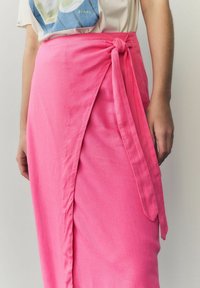 Rosa omslagsskjol gjord av lättviktig tyg, med en framknutning och en draperad design med en sidoklyfta. Slät textur, midilängd.