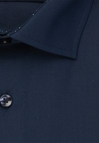 Marineblauw overhemd met knopen, voorzien van een gestructureerde kraag, sluiting met één donkere knop en een gladde textuur. Subtiele stikseldetails.