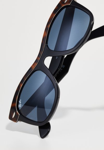 Слънчеви очила Ray-Ban Wayfarer с ръбове от черупка на костенурка и тъмносини лещи, поставени на бяла повърхност.