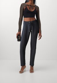 Svart crop-top med långa, glittriga ärmar och knytning. Grå byxor med dragsko och sidofickor. Klara klacksandaler, liten svart väska.