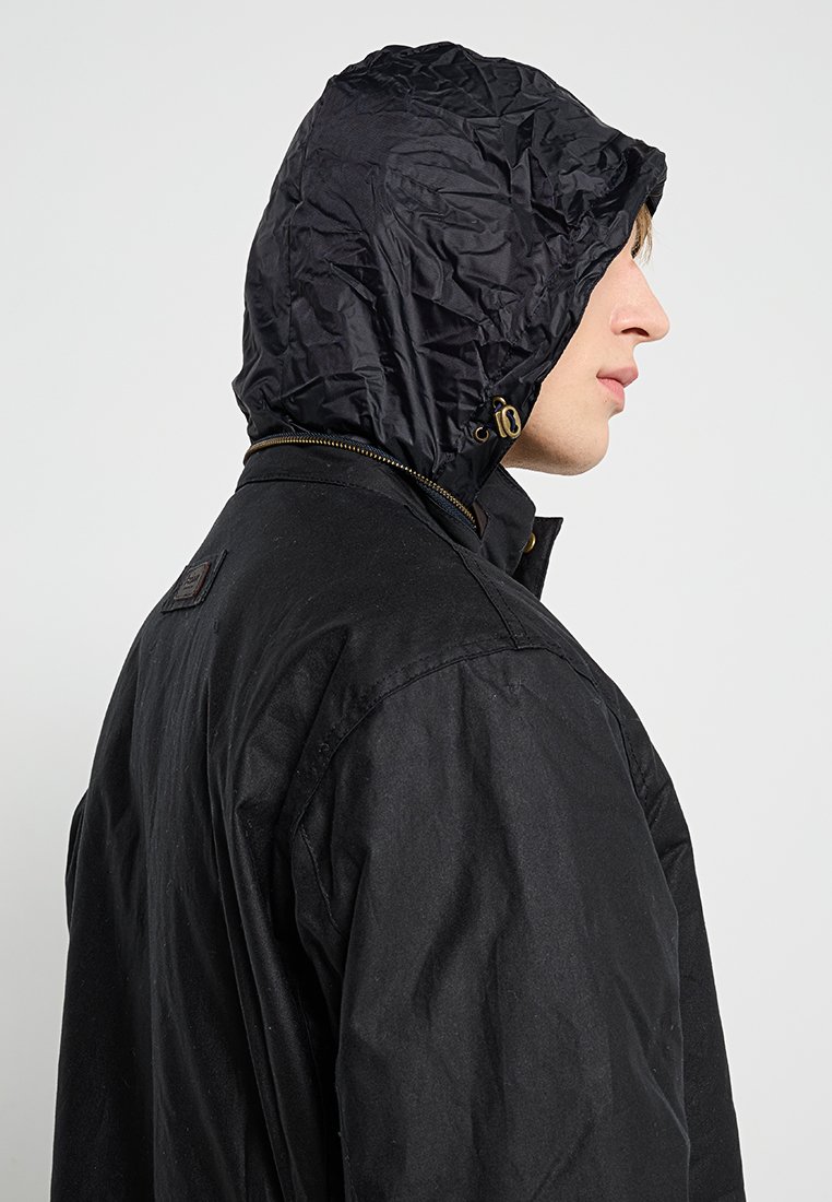 Veste noire avec une finition texturée, dotée d'une fermeture zippée à l'avant et d'une capuche en tissu froissé. La vue de côté montre des détails comme le col et la quincaillerie.