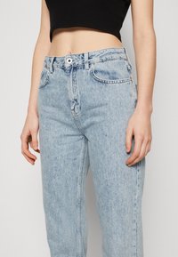 Vaqueros de tiro alto en azul claro, fabricados en denim, con cierre de botón en la parte frontal, bolsillos laterales y un diseño de pierna recta.