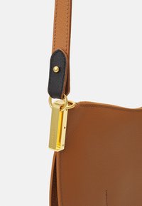 Brown leather handbag with a textured finish, featuring a black strap accent, gold hardware, and a zipper closure detail.