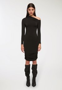 Abito nero a maniche lunghe con una spalla; silhouette aderente; dettagli arricciati all'orlo; abbinato a stivali neri a ginocchio texturizzati.