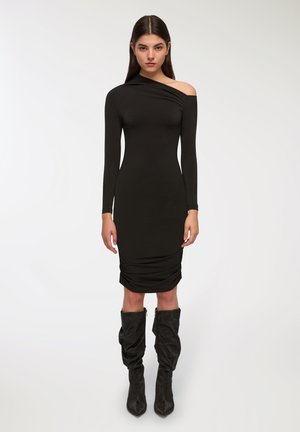 Abito nero a maniche lunghe con una spalla; silhouette aderente; dettagli arricciati all'orlo; abbinato a stivali neri a ginocchio texturizzati.