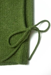 Grüner Strickstoff mit strukturierter Oberfläche, versehen mit einer gebundenen Schleifendetail. Die Farbe ist ein sattes, dunkles Grün und vermittelt ein gemütliches Erscheinungsbild.
