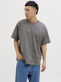 Graues kurzärmeliges T-Shirt aus weichem Stoff, runder Ausschnitt, lockere Passform, kombiniert mit hellblauen Jeans, steht vor einem schlichten Hintergrund.