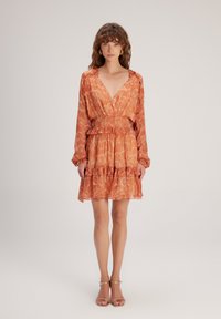 Orangen Kleid mit Muster, das einen tiefen V-Ausschnitt, lange Ärmel, einen elastischen Bund und einen rüschierten Saum aufweist. Der Stoff wirkt leicht und fließend.