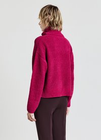 Fuchsia Strickpullover mit hohem Kragen, überschnittenen Schultern und geripptem Muster. Verkürzter Saum mit lockerer Passform, kombiniert mit dunklen Hosen.