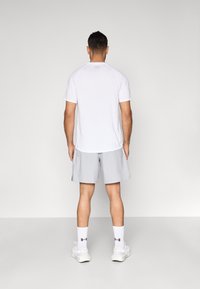 White athletic t-shirt with short sleeves, paired with light gray shorts. Worn with white socks and neutral sneakers. Simple, functional design.