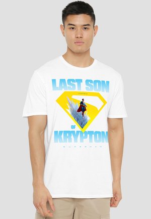 Young man wearing a white T-shirt with blue text "Last Son of Krypton" and Superman flying over ice crystals inside a yellow emblem.