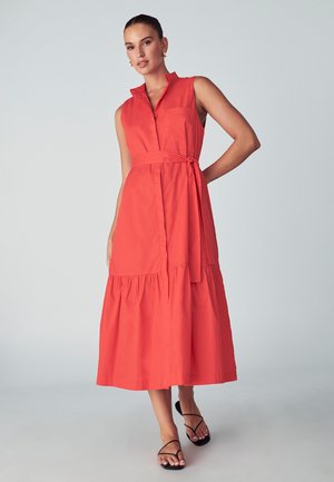Robe midi rouge sans manches avec un col, une taille cintrée et une jupe à volants. Elle présente une poche latérale et une ceinture assortie.