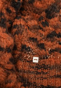 Maglione lavorato a maglia con un motivo testurizzato nelle tonalità dell'arancio bruciato e del nero, con una piccola etichetta metallica cucita nel tessuto.