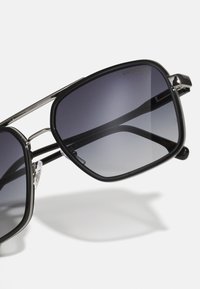 Occhiali da sole neri con montatura rettangolare, dettagli in metallo e lenti scure sfumate. Presentano para-naso trasparenti e un design elegante.