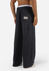 Sorte brede sweatpants med elastisk talje, en baglomme med et mærke og blød, glat tekstur.