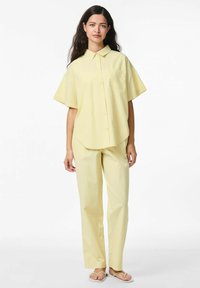 Geel gestreepte shirt met korte mouwen en een kraag, gecombineerd met bijpassende geel gestreepte broek. De stof lijkt zacht en lichtgewicht.