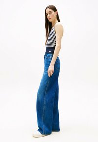 Top de tirantes a rayas con una cintura de color azul oscuro, combinado con jeans de mezclilla azul de pierna ancha. Los jeans tienen un diseño clásico de cinco bolsillos.