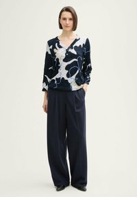 T-shirt à manches longues avec un motif abstrait bleu marine, blanc et bleu, doté d'un col en V et de détails boutons. Assorti à un pantalon foncé ample.