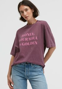 Purple cotton t-shirt with short sleeves, featuring bold text in light pink: "HONEY, YOUR SOUL IS GOLDEN." Casual, relaxed fit.