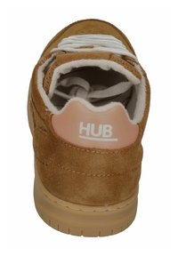 Braune Wildledersneaker von hinten betrachtet, mit weißen Schnürsenkeln und einem rosa Aufnäher mit der Aufschrift "HUB" am Schaftrand.