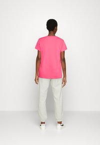 T-shirt en coton rose vif à manches courtes, associé à un pantalon de survêtement gris clair. La tenue présente une coupe décontractée et peu de détails.