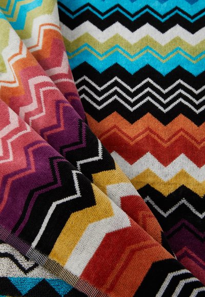 Tkanina s multicolor vzorom, ktorá obsahuje chevron pruhy v purpúrovej, oranžovej, žltej, zelenej, tyrkysovej, čiernej a bielej farbe. Mäkká textúra.