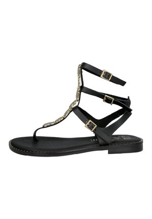 Sandalia plana negra con tres hebillas doradas, lazo para el dedo y cadena decorativa dorada que corre verticalmente a lo largo de la correa frontal.