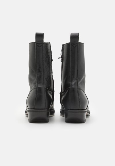 Svarta läderankelboots med en slät textur, rund tå, sydd detaljering och låg blockklack. Har bakre dragflikar.